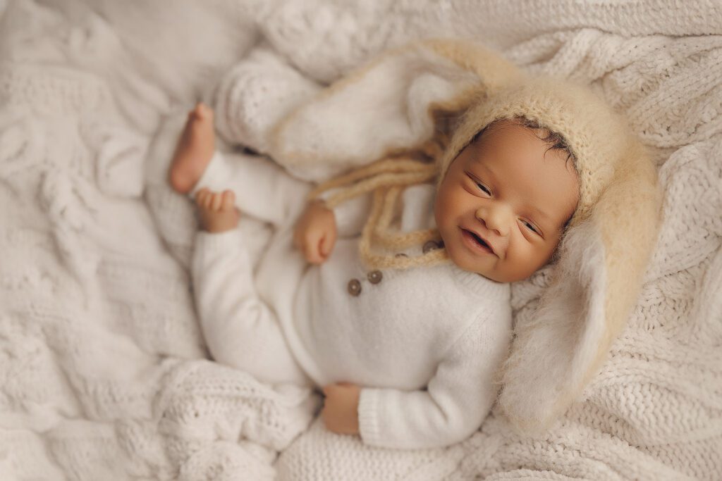Smiling newborn baby in bunny hat at photography studio.