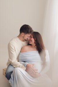 Close maternity portrait of an expectant couple embracing and smiling in a softly lit studio