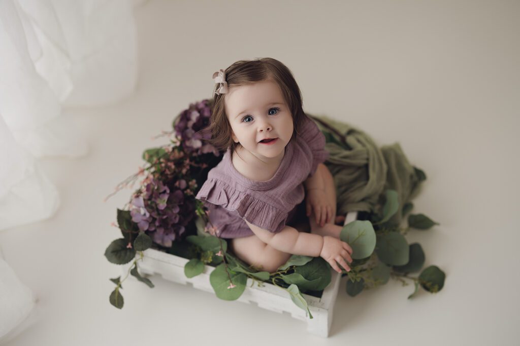 Baby girl surrounded with purple flowers in baby photography studio