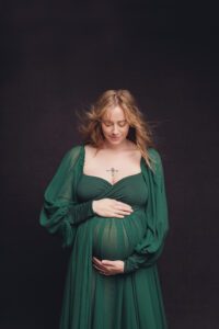 Pregnant woman posed in an emerald green gown looking down at her belly in a Frederick maternity photographer studio