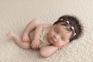 Sleeping newborn baby girl wearing a delicate headband photographed in a Baltimore newborn photography studio